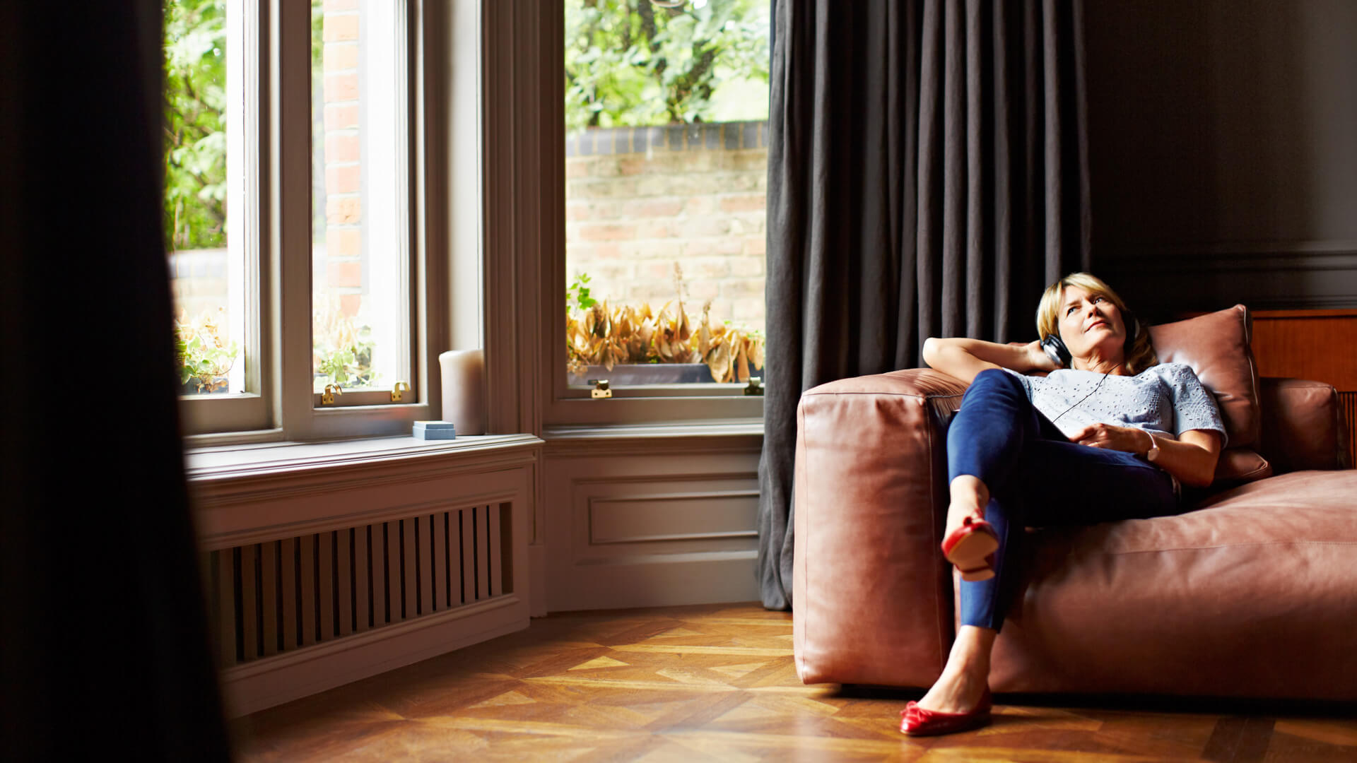 Woman On Sofa With Bay Window Listening To Music